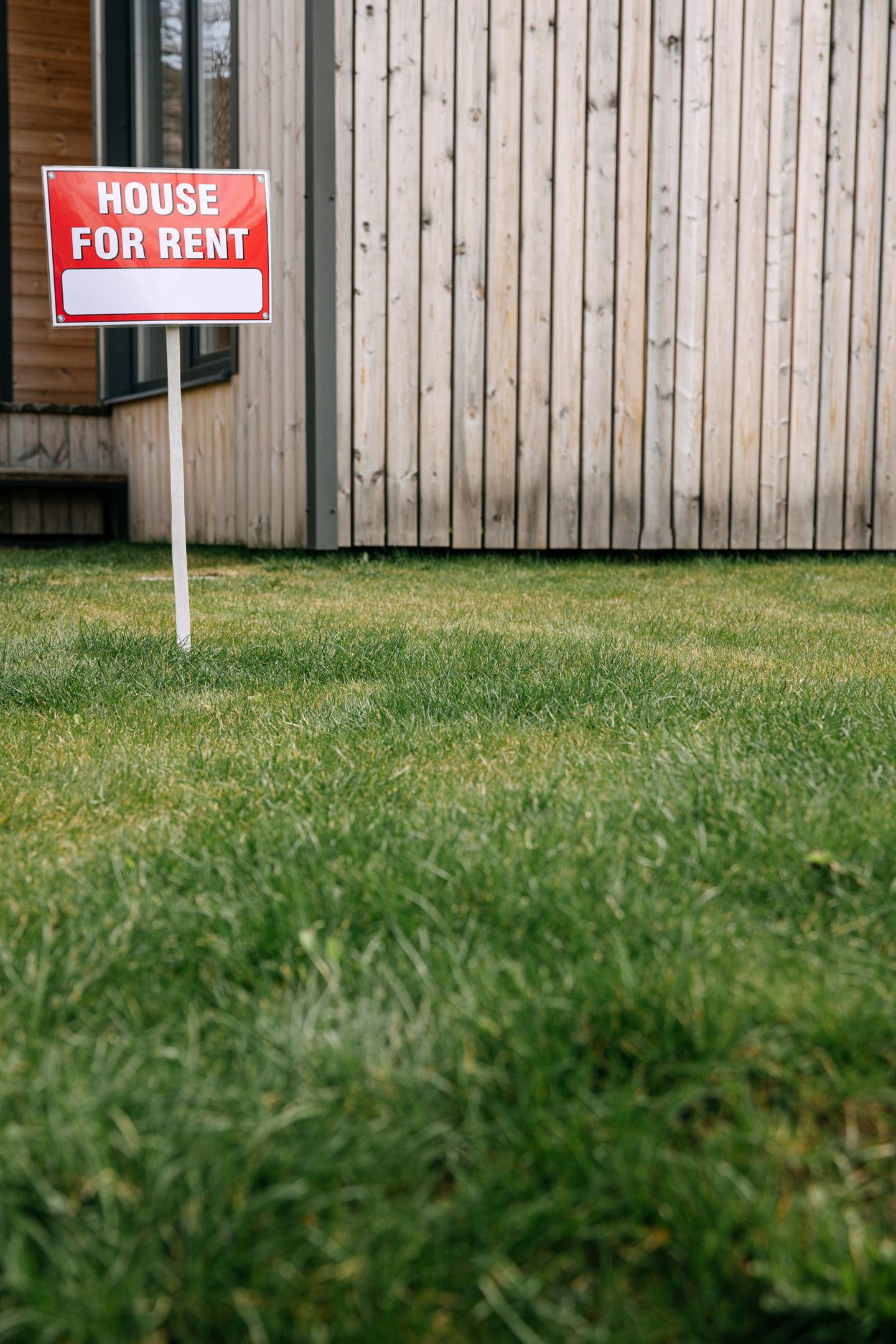 Red 'House for Rent' sign on green lawn with