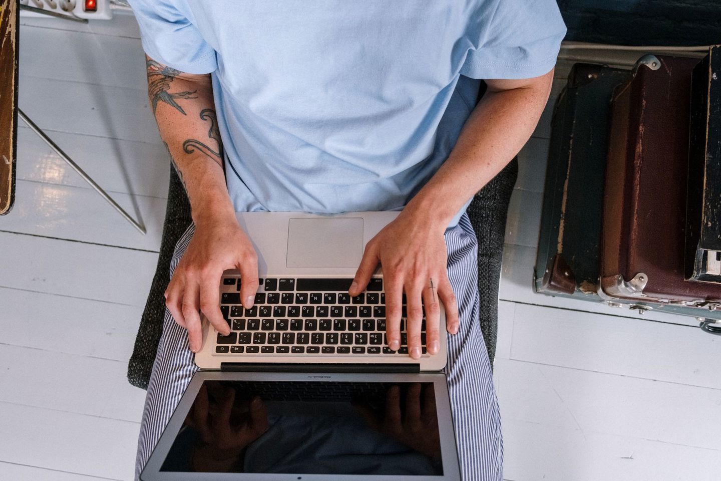 An adult with tattoos typing on a laptop indo