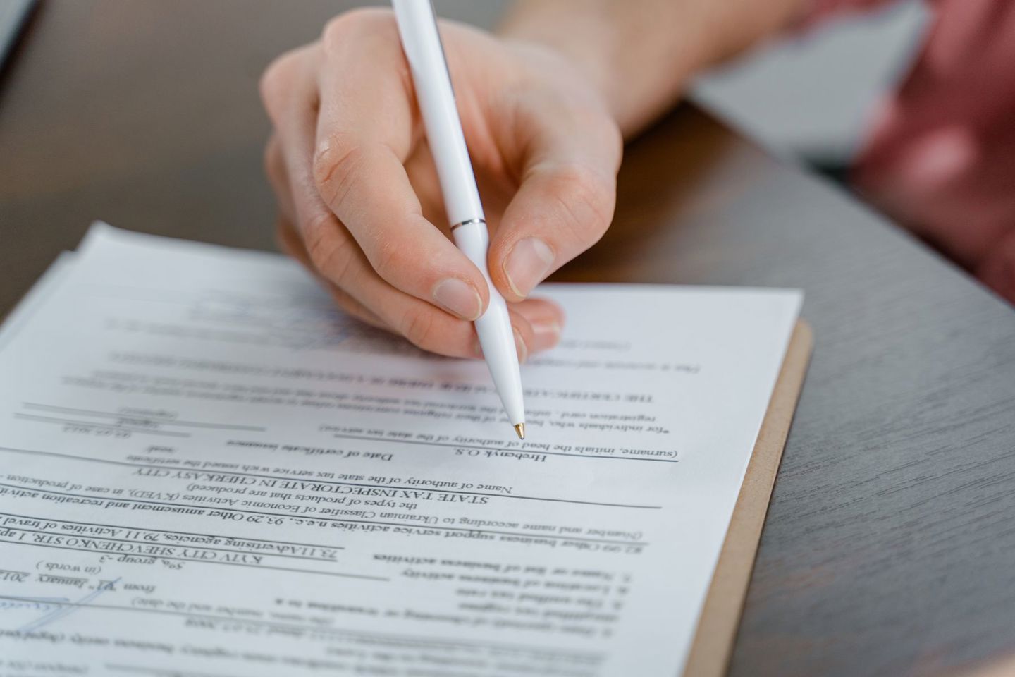 A hand holding a pen signing a document, clos